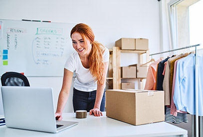 Young online business owner looking at laptop while preparing deliveries for clients